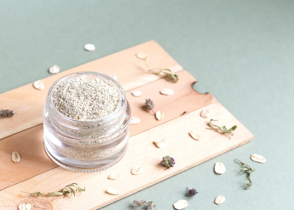 Powdered oats in a small glass jar with dried herbs like rosemary and lavender