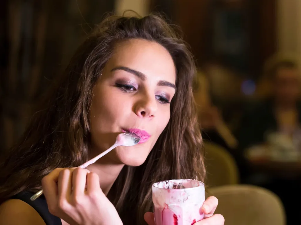 Young woman eating strawberry flavored yogurt with fruit at a cafe 
