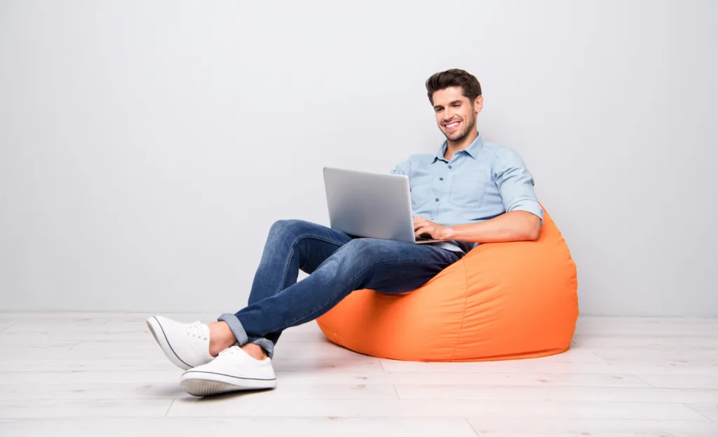 Young man on a bean bag looking at the laptop